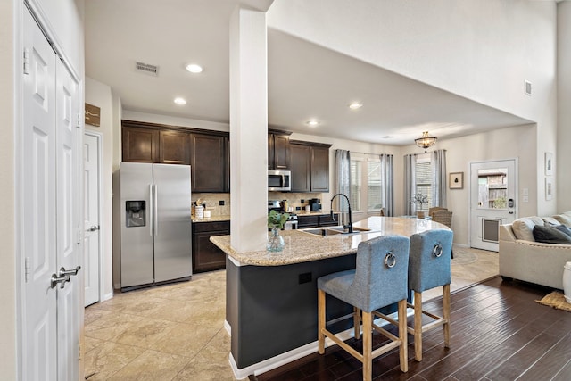 kitchen featuring dark brown cabinetry, a kitchen bar, sink, appliances with stainless steel finishes, and decorative backsplash