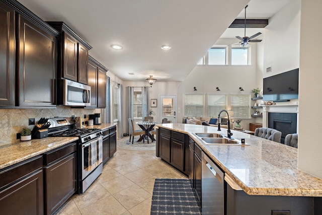 kitchen featuring tasteful backsplash, sink, stainless steel appliances, light stone countertops, and a center island with sink