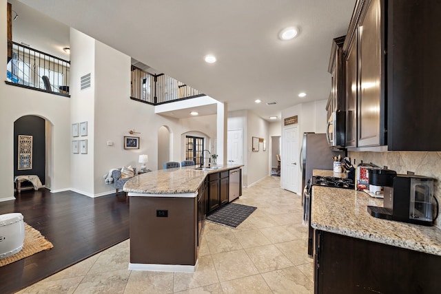 kitchen with stainless steel appliances, light stone countertops, sink, and dark brown cabinets