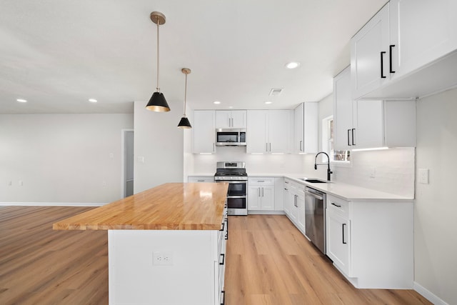 kitchen with light wood finished floors, a kitchen island, white cabinets, stainless steel appliances, and a sink