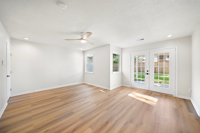 unfurnished room with visible vents, baseboards, light wood-type flooring, french doors, and a textured ceiling