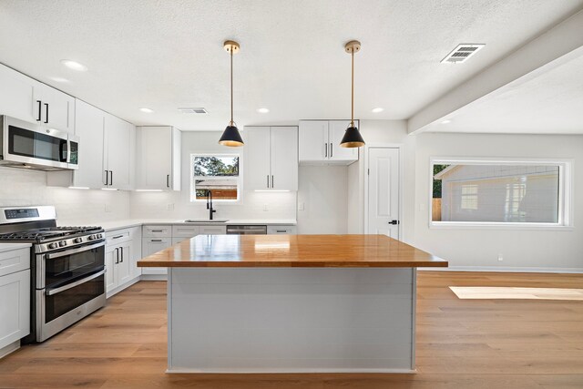 kitchen featuring stainless steel appliances, white cabinetry, sink, and pendant lighting