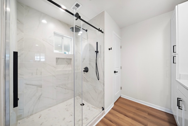 bathroom with visible vents, wood finished floors, a marble finish shower, baseboards, and vanity