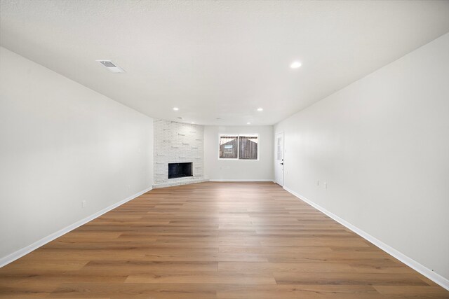 unfurnished living room with light wood finished floors, visible vents, a brick fireplace, baseboards, and recessed lighting