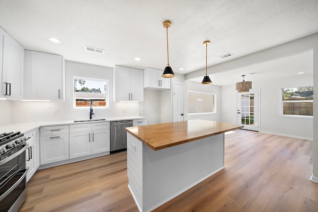 kitchen featuring visible vents, light wood-type flooring, white cabinets, stainless steel appliances, and a sink