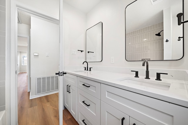 bathroom with a sink, visible vents, wood finished floors, and double vanity