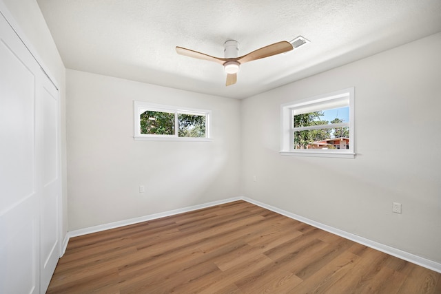 spare room with ceiling fan, hardwood / wood-style floors, a textured ceiling, and a wealth of natural light