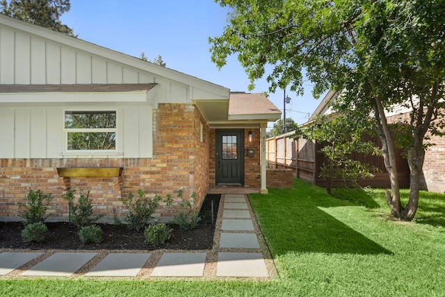 entrance to property with board and batten siding, fence, a lawn, and brick siding