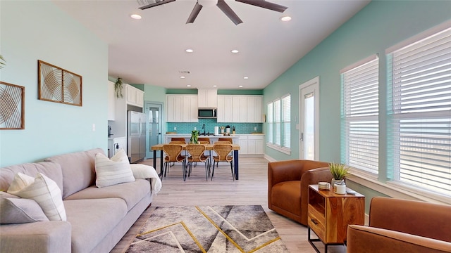 living room featuring ceiling fan, sink, and light wood-type flooring