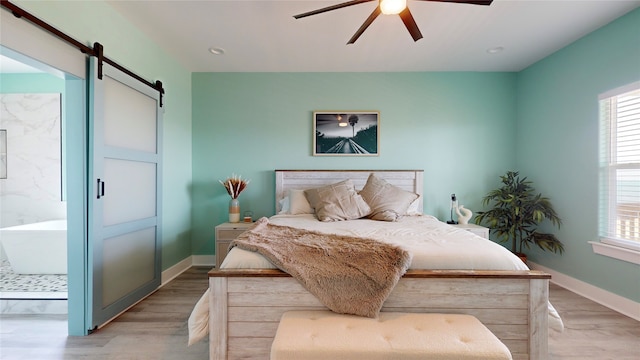 bedroom with multiple windows, light hardwood / wood-style flooring, a barn door, and ceiling fan