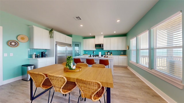 kitchen featuring appliances with stainless steel finishes, white cabinetry, a kitchen breakfast bar, tasteful backsplash, and a center island with sink