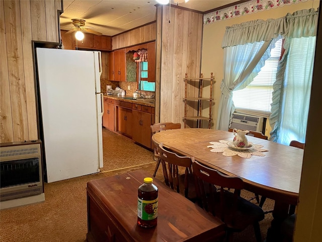 carpeted dining room with heating unit, cooling unit, wooden walls, and ceiling fan