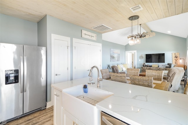 kitchen featuring decorative light fixtures, lofted ceiling with beams, sink, stainless steel fridge, and light stone counters