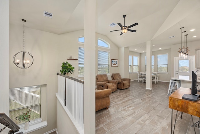 living room with ceiling fan with notable chandelier, light hardwood / wood-style flooring, and vaulted ceiling