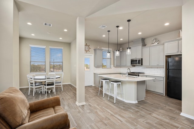 kitchen featuring a breakfast bar, appliances with stainless steel finishes, hanging light fixtures, backsplash, and an island with sink