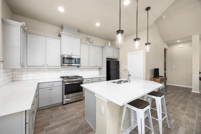 kitchen with sink, pendant lighting, stainless steel appliances, a kitchen island with sink, and backsplash