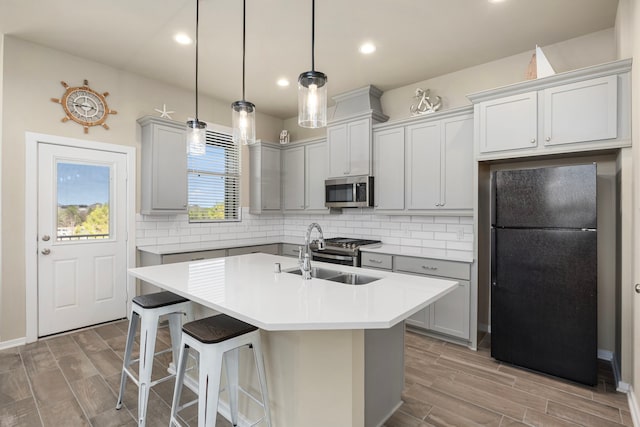 kitchen with sink, appliances with stainless steel finishes, pendant lighting, a kitchen island with sink, and decorative backsplash