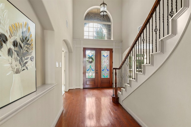 foyer with french doors, wood-type flooring, an inviting chandelier, and a high ceiling