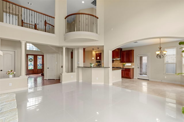 unfurnished living room with light tile patterned flooring, a chandelier, and ornate columns