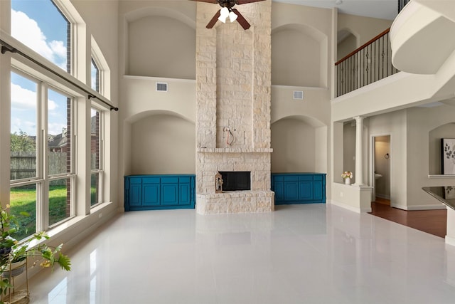 unfurnished living room with a high ceiling, a stone fireplace, and ceiling fan