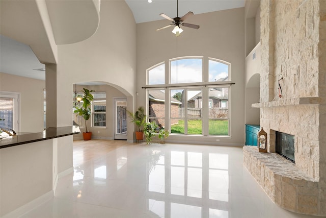 unfurnished living room featuring a high ceiling, a stone fireplace, and ceiling fan