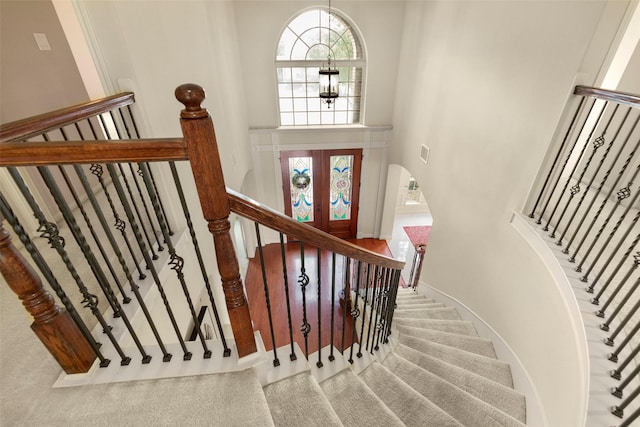 stairway featuring a towering ceiling, a notable chandelier, and french doors