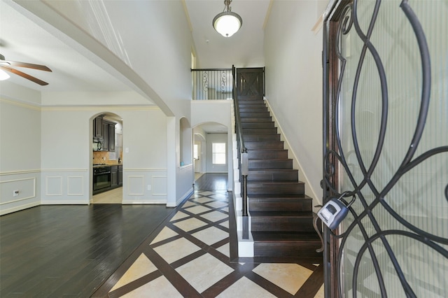 foyer entrance featuring hardwood / wood-style floors, crown molding, ceiling fan, and a high ceiling