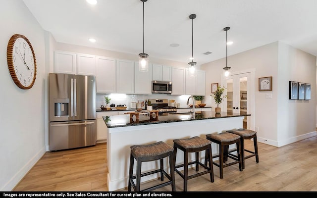 kitchen featuring appliances with stainless steel finishes, white cabinetry, tasteful backsplash, an island with sink, and dark stone counters