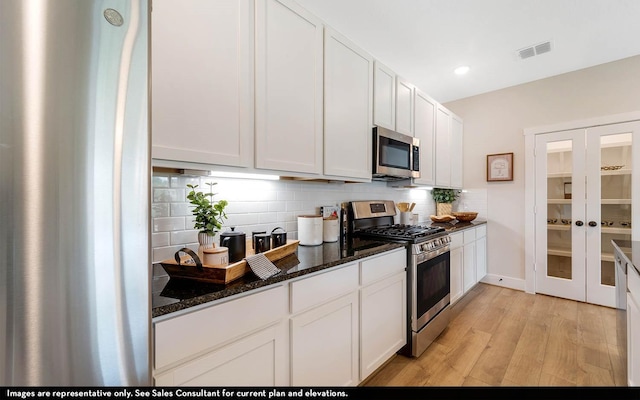 kitchen featuring white cabinetry, backsplash, stainless steel appliances, and dark stone counters