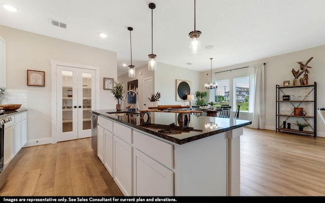 kitchen featuring french doors, sink, hanging light fixtures, a center island with sink, and white cabinets