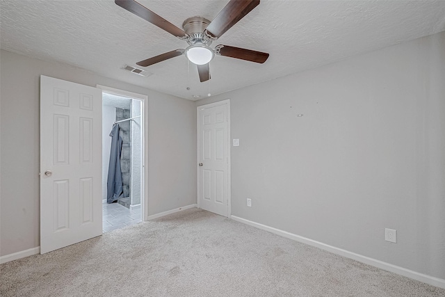 unfurnished bedroom with a walk in closet, ceiling fan, light carpet, a textured ceiling, and a closet