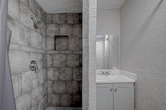 bathroom featuring vanity, a textured ceiling, and tiled shower