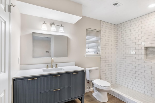 bathroom featuring vanity, toilet, hardwood / wood-style floors, and a tile shower