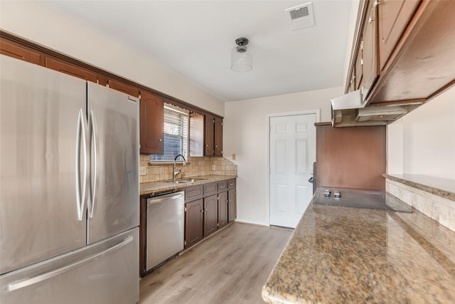 kitchen featuring sink, light hardwood / wood-style flooring, dark stone countertops, appliances with stainless steel finishes, and backsplash