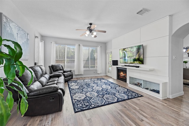 living room featuring ceiling fan, a textured ceiling, and light hardwood / wood-style floors