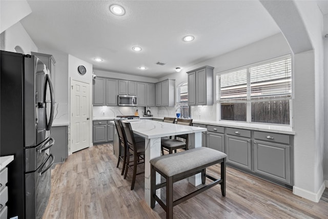 kitchen featuring appliances with stainless steel finishes, gray cabinetry, light hardwood / wood-style floors, and decorative backsplash