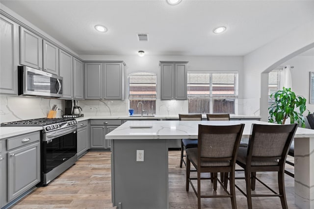 kitchen with a breakfast bar area, a center island, light hardwood / wood-style flooring, gray cabinets, and stainless steel appliances