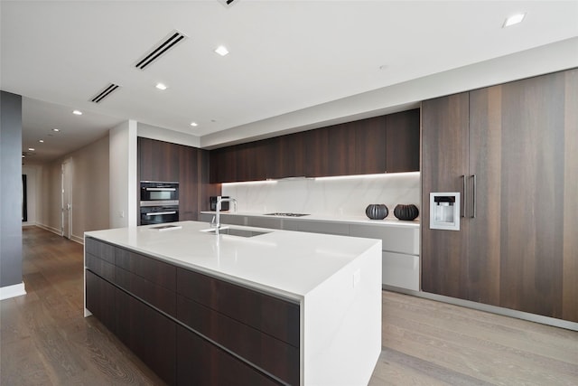 kitchen featuring sink, backsplash, light hardwood / wood-style floors, and a center island with sink