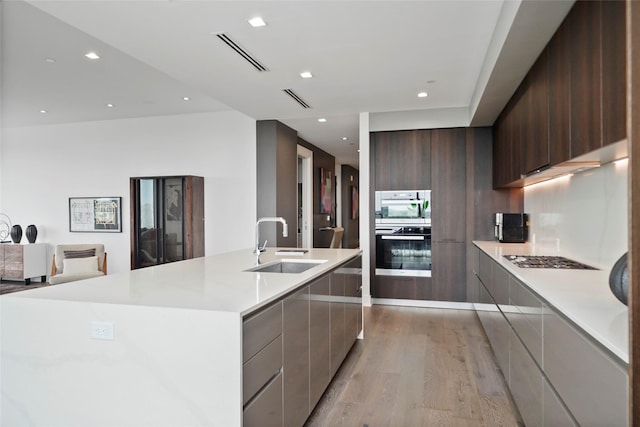 kitchen with a spacious island, sink, dark brown cabinets, light hardwood / wood-style flooring, and appliances with stainless steel finishes