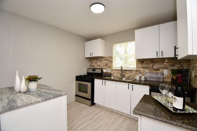 kitchen featuring stainless steel gas range oven, sink, white cabinets, and decorative backsplash