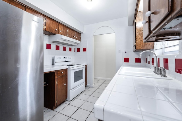 kitchen featuring tile countertops, stainless steel fridge, backsplash, light tile patterned floors, and electric stove