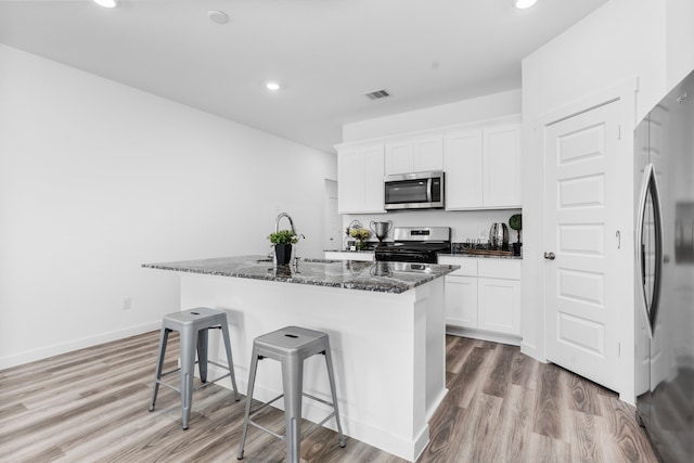 kitchen featuring a breakfast bar, white cabinets, dark stone counters, a kitchen island with sink, and stainless steel appliances