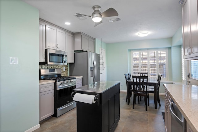 kitchen featuring a kitchen island, appliances with stainless steel finishes, backsplash, light tile patterned floors, and ceiling fan