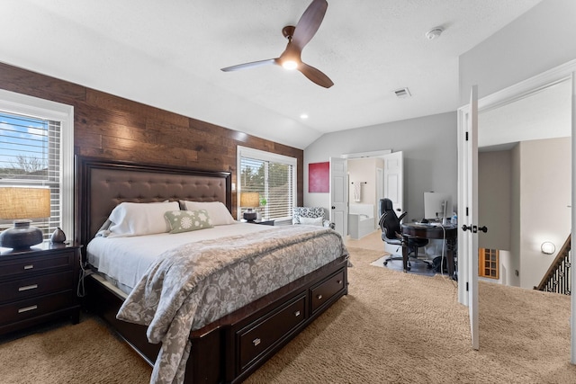 carpeted bedroom with lofted ceiling, connected bathroom, a textured ceiling, wooden walls, and ceiling fan