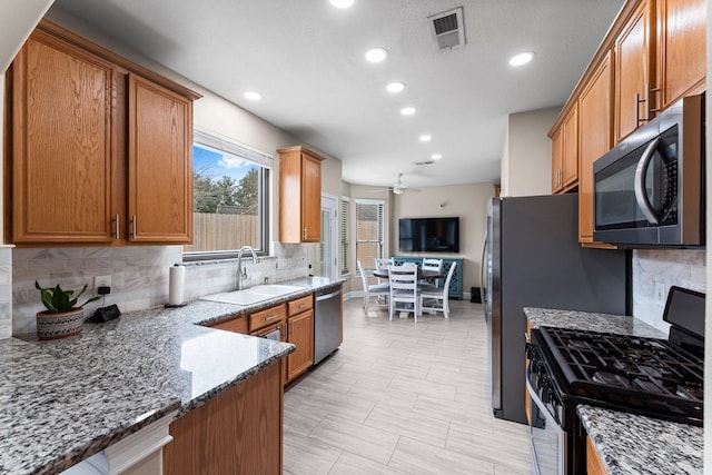 kitchen with light stone countertops, backsplash, stainless steel appliances, and sink