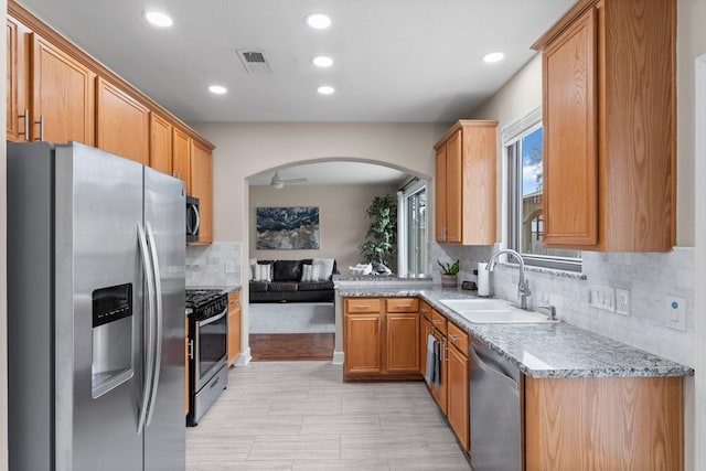 kitchen featuring sink, decorative backsplash, ceiling fan, stainless steel appliances, and light stone countertops