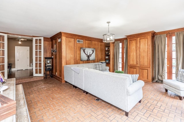 living room featuring french doors, a notable chandelier, and wood walls