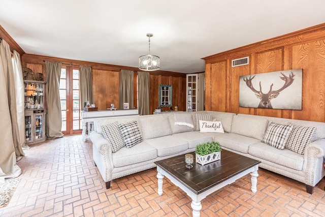 living room featuring wooden walls, french doors, and a chandelier