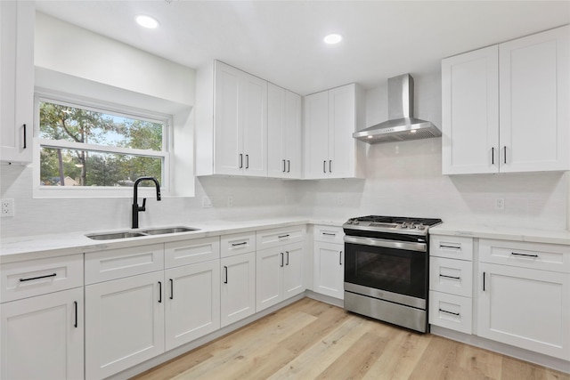 kitchen featuring sink, white cabinets, light stone counters, stainless steel gas range oven, and wall chimney exhaust hood