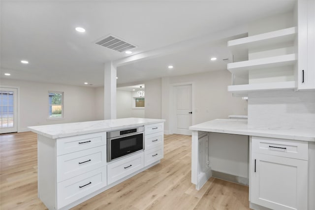 kitchen featuring white cabinetry, light stone countertops, light hardwood / wood-style floors, and decorative backsplash